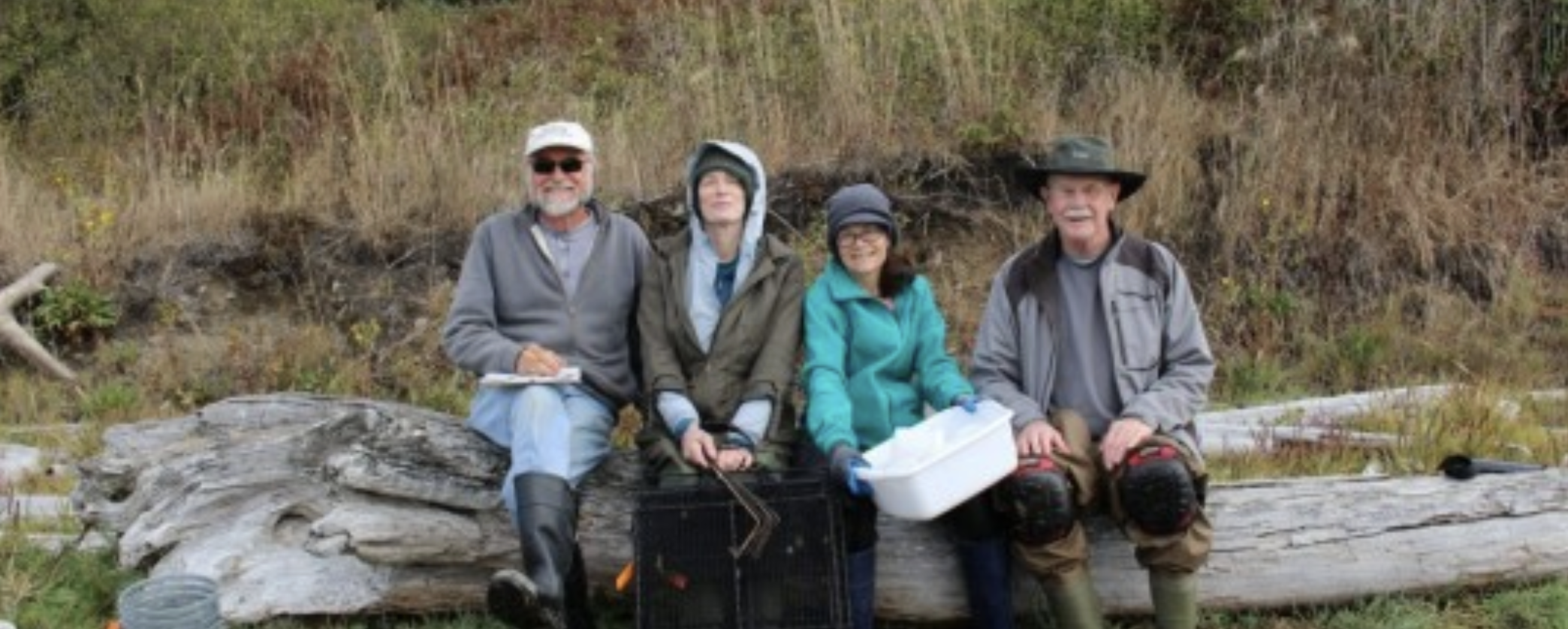 4 crabbers sit together on a log at Penn Cove