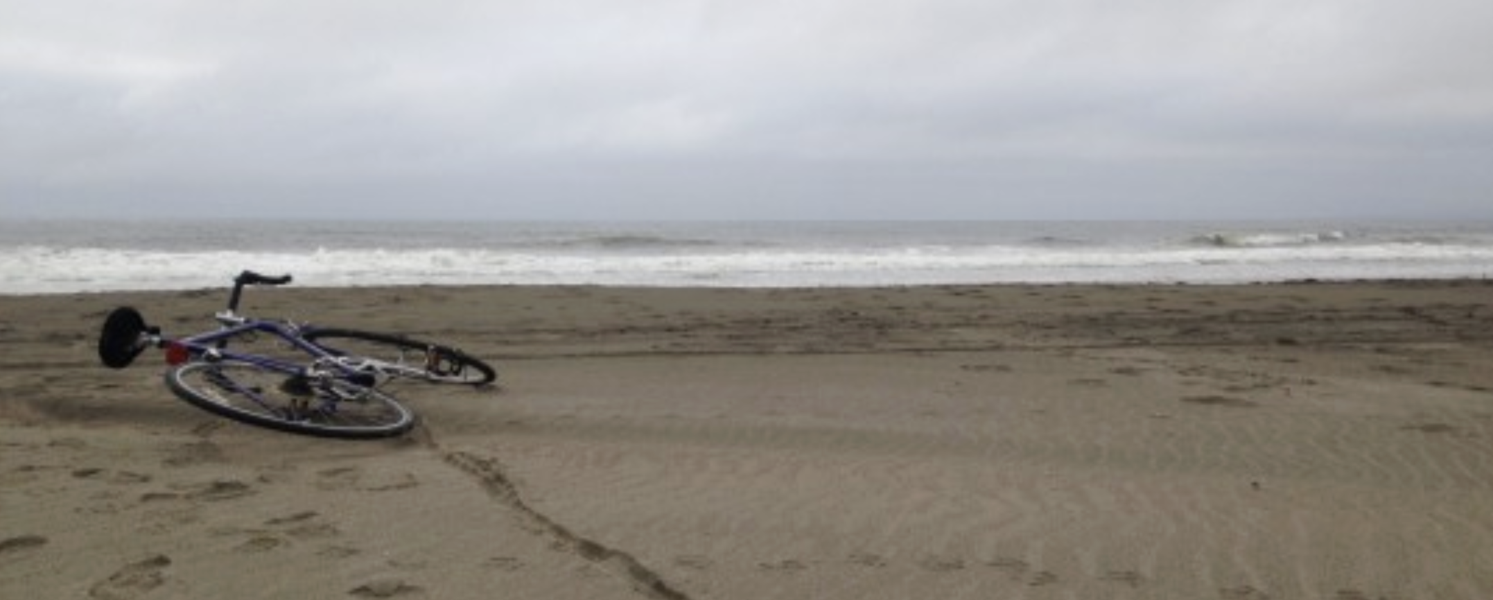 Cloudy day at the beach with a bike laying in the sand