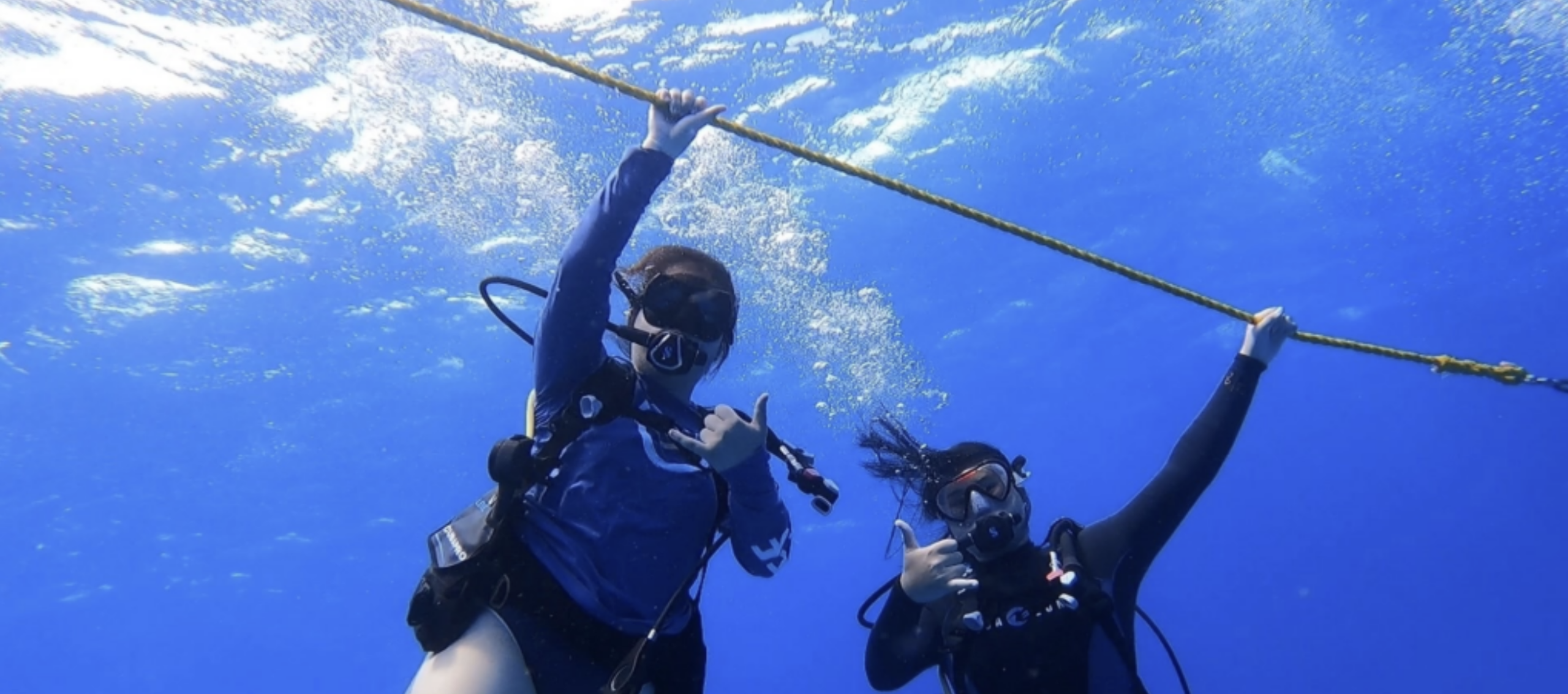 Aina (on the left) and her sister (on the right) in the water with scuba gear holding onto the anchor rope.<br />
